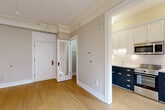 Located in the heart of Portland's SW Broadway corridor, this well-appointed unit offers a thoughtful layout across a single floor, comprising a living room, kitchen, and bathroom. The living room is bright and open, featuring warm hardwood flooring, crown molding, and a classic cast-iron radiator that adds vintage character. Large French doors with a decorative transom allow natural light to fill the space while offering views to an outdoor balcony. A ceiling fan adds both style and function overhead. The kitchen is a standout feature, showcasing a bold two-tone design with navy lower cabinetry, white upper cabinets, white subway tile backsplash, and light stone countertops. Stainless steel appliances — including a built-in microwave, range, and refrigerator — complete the modern, functional setup. The bathroom retains its classic charm with white penny tile flooring, full subway tile walls accented by a teal border stripe, a pedestal sink, and a soaking tub with shower. A frosted window provides natural light while maintaining privacy. Throughout the unit, consistent hardwood flooring, neutral warm-toned walls, and crisp white trim create a cohesive and inviting aesthetic.