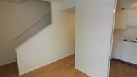 This two-floor space presents a straightforward and functional design with a clean, minimalist aesthetic throughout. The interior is characterized by bright white walls that create a fresh and open atmosphere, complemented by warm-toned hardwood flooring that runs throughout the lower level, adding a natural and inviting feel underfoot.

A staircase connects the two floors, and the area beneath the stairs reveals an additional nook or passageway, making practical use of the available space. The layout is open and uncluttered, allowing for flexible use and easy customization to suit a variety of needs.

The main level features a well-proportioned room with a neutral color palette, enhanced by the light-toned flooring and smooth wall finishes. A doorway or opening leads into an adjacent area, suggesting a connected flow between spaces on the ground floor. Electrical outlets and light switches are neatly integrated into the walls, maintaining the clean lines of the interior.

Overall, the space offers a blank-canvas quality — move-in ready and versatile — with its simple finishes and practical two-level configuration providing a solid foundation for personalization and furnishing.