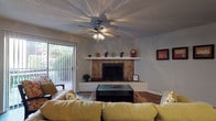 This single-floor, 2-bedroom, 2-bathroom residence offers a thoughtfully arranged layout with a variety of functional and comfortable living spaces. The living room serves as the heart of the home, featuring a tile-surround wood-burning fireplace with a white mantle shelf, rich hardwood flooring, a textured ceiling, a ceiling fan with light fixture, and a sliding glass door that fills the space with natural light and provides access to an outdoor area. Built-in shelving adds a decorative architectural touch to the living area.

The galley-style kitchen is equipped with white cabinetry, dark granite-style countertops, black appliances including an electric range and dishwasher, a double sink, and a skylight that brightens the space naturally. Hardwood flooring continues throughout.

Both bedrooms are carpeted and feature ceiling fans, vertical blinds, and sliding glass doors leading to private outdoor spaces. The primary bedroom includes a large dresser with a mirror. The second bedroom is bright and open, with a window overlooking greenery.

Each bathroom is appointed with white cabinetry, granite-style countertops, large vanity mirrors with overhead lighting, and shower-tub combinations with curtains. One bathroom features hardwood flooring, while the other offers a clean, functional layout adjacent to the primary bedroom.