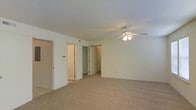 This single-floor residential space presents a clean, functional layout designed for comfortable everyday living. The main living area is finished with wall-to-wall neutral-toned carpeting, providing a warm and cohesive feel underfoot throughout the space. A ceiling fan with an integrated light fixture is centrally mounted overhead, offering both ambient lighting and air circulation to keep the space comfortable year-round. The walls are finished in a crisp, light neutral tone that contributes to a bright and open atmosphere. Multiple doorways are visible from the main living area, providing access to additional rooms and generous closet storage, suggesting a practical and well-organized floor plan. The closet spaces appear spacious and easily accessible, adding to the overall utility of the home. The layout flows naturally between areas, making the space feel connected and easy to navigate. With its neutral finishes, soft carpeting, and thoughtful storage options, this single-floor residence offers a versatile and move-in-ready environment suitable for a variety of living arrangements.