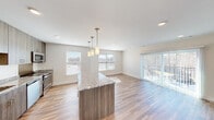This single-floor unit offers a thoughtfully designed open-concept layout that seamlessly connects the kitchen, dining, and living areas. Light wood-tone flooring runs throughout, complementing the neutral, warm-white walls and recessed lighting that keep the space bright and airy.

The kitchen is well-appointed with floor-to-ceiling wood-grain cabinetry, granite countertops, and a full suite of stainless steel appliances including a refrigerator, range, microwave, and dishwasher. A central island with a granite surface and matching cabinetry provides additional prep space and serves as a natural divider between the kitchen and the open living area. Pendant lighting above the island adds a stylish focal point.

The living area is generously proportioned, with multiple windows that invite natural light and sliding glass doors that open to an outdoor balcony, offering views of the surrounding area. The bedrooms continue the hardwood-style flooring and feature windows with exterior views.

The bathrooms are clean and functional, with one featuring a walk-in glass-enclosed shower with brushed nickel fixtures and built-in shelving, and another offering a full soaking tub and shower combination. Overall, the space presents a contemporary, move-in-ready aesthetic with quality finishes throughout.