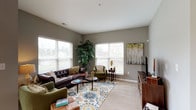 Located at 6249 Walton Breck Way in Westerville, Ohio, this single-floor residence offers a thoughtfully designed layout with comfortable living spaces throughout. The living room is generously sized and bathed in natural light from multiple large windows dressed with white blinds. Neutral gray walls and plush carpeting create a warm, welcoming atmosphere, complemented by ample room for seating arrangements. The kitchen is well-equipped with rich dark-stained cabinetry, light stone countertops, black appliances, and wood-look flooring. A peninsula with seating for two provides a casual dining option, while pendant lighting adds a polished touch. A sliding glass door connects the kitchen area to the outdoors, allowing natural light to pour in. The bedroom is a serene retreat featuring soft carpeting, cool-toned gray walls, and a window that brings in natural light. It connects directly to a full bathroom, which includes a dark wood vanity with a stone countertop, wood-look tile flooring, and access to a walk-in closet with built-in shelving. A dedicated office or den area is also present, adding functional versatility to the floor plan. Overall, the space presents a cohesive, modern aesthetic with consistent finishes and a comfortable, livable design throughout.