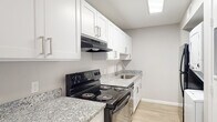 This single-floor residence offers a thoughtfully updated interior with a clean, neutral aesthetic throughout. The open living area is finished with light wood-style flooring that extends seamlessly across the space, complemented by soft gray walls and crisp white trim. A ceiling fan with integrated lighting serves as a functional centerpiece, while a window fitted with horizontal blinds allows natural light to filter in, enhancing the airy feel of the room.

The kitchen is designed in a galley layout, featuring white shaker-style cabinetry with brushed nickel hardware and granite-look countertops. A black electric range with a range hood sits alongside a stainless steel sink, and a skylight overhead adds additional brightness to the workspace. Notably, the kitchen also accommodates a stacked in-unit washer and dryer, providing added convenience.

The bedrooms continue the consistent flooring and neutral palette, each equipped with ceiling fans and closet storage. Multiple doorways and open closet configurations offer practical storage solutions. The overall design prioritizes functionality and a cohesive, move-in-ready appearance, with clean finishes and consistent materials tying the entire space together.