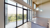Located at 299 Debaliviere Ave in St. Louis, Missouri, this two-story residence offers a striking blend of modern design and open, airy living. The main living area commands immediate attention with its dramatic double-height ceilings and an expansive wall of floor-to-ceiling black-framed windows and glass doors that open onto a private balcony, flooding the space with natural light and offering sweeping views of the surrounding treetops and cityscape. Light-toned hardwood flooring flows throughout, complementing the warm neutral palette of the walls.

The kitchen is outfitted with stainless steel appliances, dark gray shaker-style cabinetry, a decorative tile backsplash, and dark stone countertops, creating a refined and functional workspace. A dedicated island provides additional prep and serving space.

The upper level accommodates the private quarters, accessible via an interior staircase. Bedrooms are generously proportioned with continued hardwood flooring and ample natural light. The bathrooms are well-appointed, featuring a dual-sink vanity with dark cabinetry and matte black fixtures in the primary bath, and a full soaking tub with tiled surround in the secondary bath. Bold navy-toned interior doors add a contemporary design accent throughout the home.