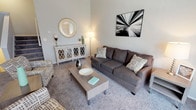 This two-story, 2-bedroom, 1.5-bathroom home offers a well-designed layout with comfortable living spaces spread across two levels. The living room is a welcoming focal point, featuring soaring vaulted ceilings, soft carpet flooring, and a large sliding glass door fitted with vertical blinds that floods the room with natural light. The kitchen is efficiently designed with white cabinetry, granite-style countertops, a stainless steel sink, and light wood-look flooring, providing a clean and functional workspace. Adjacent to the kitchen, the dining area offers an intimate setting with room for a full dining table, accented by neutral walls. The primary bedroom is generously sized with plush carpet, a natural light-filled window, and ample closet space. The second bedroom is a flexible space, equally suited as a guest room or home office, with carpet flooring and a bright window. The full bathroom features a tub-shower combination, while the half bath includes a dark wood vanity and light wood-look flooring. Throughout the home, neutral gray tones and clean finishes create a cohesive and modern aesthetic that is both practical and inviting.