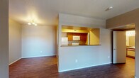 This single-floor residence is thoughtfully laid out to maximize functionality and flow. The living area serves as the central hub of the space, featuring durable hardwood-style flooring, a ceiling fan, and a tiled entryway near the front door. A sliding glass door opens to a private patio, allowing natural light to fill the room. The transition between carpet and hard flooring delineates distinct zones within the open layout.

The kitchen is positioned behind a half-wall pass-through, offering visual connectivity to the living area while maintaining a defined cooking space. It is equipped with warm-toned wood cabinetry, laminate countertops, a coil-burner electric range, over-the-range microwave, and a refrigerator. Adjacent to the kitchen, a dedicated laundry area accommodates a washer and dryer.

The bedrooms are carpeted and each include a ceiling fan. One bedroom features a window with vertical blinds and closet access, while another opens directly to the hallway with ample wall space for furnishings.

The bathroom includes a wide vanity with a single sink, laminate countertop, a large mirror with overhead lighting, and a separate toilet and shower area with hardwood-style flooring throughout.