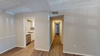 This single-floor residence offers a thoughtfully designed layout that balances comfort and functionality throughout. The living area features wood-look flooring and neutral-toned walls, with a sliding glass door that fills the space with natural light and provides direct access to the outdoors. A dedicated entryway leads seamlessly into the open living and dining areas, which transition naturally into the kitchen. The kitchen is outfitted with white shaker-style cabinetry, light stone countertops, a stainless steel electric range with an overhead ventilation hood, and a dishwasher — combining both style and practicality. A central hallway connects the private areas of the home, leading to multiple bedrooms. The bedrooms feature plush carpet flooring, neutral walls, natural light from windows, and built-in closets with louvered bifold doors for convenient storage. Two full bathrooms serve the home, each featuring a tub-shower combination with white tile surround, wood-look flooring, and white vanity cabinetry. One bathroom includes grab bars for added accessibility. Textured ceilings are consistent throughout the home, complementing the clean, understated aesthetic of the overall space.