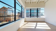 Located at 25 Van Dyke Ave in Hartford, CT, this single-floor residence showcases a compelling blend of industrial character and modern finishes throughout its open layout. Soaring ceilings with exposed white-painted structural beams lend an airy, loft-like quality to the living spaces, while large black-framed floor-to-ceiling windows flood the interior with abundant natural light and frame views of Hartford's historic surrounding architecture, including neighboring brick buildings and city landmarks.

The open-concept living area features light hardwood-style flooring that extends throughout, complementing the bright white walls and creating a clean, cohesive aesthetic. The kitchen is a standout feature, equipped with slate-blue cabinetry, white quartz countertops, a large center island with an integrated sink, stainless steel appliances including a range, microwave, refrigerator, and dishwasher, white subway tile backsplash, and industrial-style pendant lighting overhead. A window-facing position within the kitchen allows for natural light while cooking.

The bathroom offers a functional, well-appointed design with large-format neutral tile flooring, a soaking tub, toilet, and a wood-toned vanity with a clean white countertop. The overall ambiance of the space is bright, modern, and urban, with thoughtful design details that honor the building's industrial heritage.