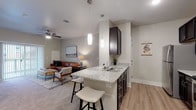 This single-floor residence offers a thoughtfully designed open-concept layout that seamlessly connects the kitchen, dining, and living areas. The kitchen is outfitted with dark espresso cabinetry, granite countertops, stainless steel appliances — including a refrigerator, range, and microwave — and a peninsula with bar seating illuminated by pendant lighting. Light wood-style flooring extends throughout the kitchen and main areas, lending warmth and continuity to the space.

The living room is generously sized and carpeted, featuring a ceiling fan, sliding glass doors that open to an outdoor space, and ample room for both a seating and dining arrangement. Natural light filters in through the sliding doors, enhancing the open, airy feel of the room.

The bedroom is a comfortable retreat, also carpeted, with multiple windows allowing natural light, a ceiling fan, and a dedicated closet. The neutral color palette and soft finishes create a calm, restful ambiance.

The bathroom features dark cabinetry with a granite-topped vanity, a large mirror with overhead lighting, and a shower-tub combination with a curtain. Light tile flooring ties together the clean, functional design.

A dedicated in-unit laundry closet with a full-size washer and dryer adds practical convenience to this well-rounded residence.