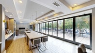 Located at 131 Poindexter Drive in Charlotte's vibrant South End neighborhood, this thoughtfully designed single-floor space offers a seamless blend of functionality and contemporary elegance. Light wood-look tile flooring flows throughout, unifying the open layout under tray ceilings with recessed lighting that create architectural depth and warmth.

The gourmet kitchen is a centerpiece of the space, anchored by an expansive white quartz island with bar seating for numerous guests. Dark cabinetry contrasts sharply against white surfaces, while stainless steel appliances — including a built-in refrigerator, double wall ovens, and a professional range hood — provide a fully equipped culinary experience. Sculptural gold globe pendant lights add a refined, artistic touch overhead.

The adjoining dining and kitchen area transitions into a dedicated dining room, where a large wooden table seats many guests beneath a tray ceiling. French doors open to an outdoor terrace, flooding the area with natural light and providing direct access to exterior amenities. A wall-mounted television and a geometric moss art piece complete the sophisticated décor.

The living room features a sleek linear fireplace set into a floor-to-ceiling tile surround, flanked by plush seating arrangements over patterned area rugs. Bold curated artwork adorns the walls, while large glass doors frame views of the surrounding greenery, reinforcing the seamless indoor-outdoor connection throughout this upscale communal space.