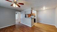 This single-floor residence offers a well-organized and functional layout with consistent wood-look flooring flowing throughout the living areas, kitchen, and bedrooms. The open-concept living area is spacious and bright, featuring a ceiling fan with light fixture, textured ceilings, and a large window fitted with vertical blinds that allows natural light to fill the room. Neutral gray walls provide a clean, modern backdrop throughout the unit.

The kitchen is designed in a galley style and is accessible via a half-wall peninsula that doubles as a breakfast bar with granite countertops. Rich, warm-toned cabinetry lines both walls of the kitchen, complemented by a mosaic tile backsplash, granite countertops, and black appliances including a refrigerator, range, and dishwasher. Recessed lighting above the kitchen ensures ample illumination for meal preparation.

The bedroom is a comfortable, well-proportioned room with its own ceiling fan, darker accent wall, and direct access to a walk-in closet, providing generous storage. The bathroom features a full tub-shower combination with white subway tile surround, maintaining a clean and classic aesthetic. Overall, the space presents a cohesive design with practical finishes and a comfortable, livable ambiance throughout.