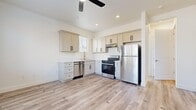 This thoughtfully designed single-story, one-bedroom, one-bathroom unit offers an efficient and modern living environment with consistent, high-quality finishes throughout. Light-toned luxury vinyl plank flooring runs seamlessly across all rooms, lending the space a clean, cohesive aesthetic.

The kitchen is a standout feature, outfitted with shaker-style cabinetry in a soft off-white finish, complemented by matte black hardware. Stainless steel appliances include a gas range, built-in dishwasher, and full-size refrigerator, alongside light-toned countertops and a sink positioned beneath a window for natural light. A ceiling fan overhead adds comfort to the open kitchen area.

The bedroom offers a well-proportioned layout with two windows fitted with horizontal blinds, allowing ample natural light while maintaining privacy. A ceiling fan provides additional ventilation, and the room connects to a dedicated closet with built-in shelving and hanging rods for organized storage.

The bathroom features a shaker-style vanity with an integrated sink, a framed mirror, sliding glass shower enclosure, and coordinating matte black fixtures, maintaining the modern design language found throughout the unit.

A hallway connects the living areas, contributing to a logical and functional floor plan. Crisp white walls and recessed lighting complete the clean, contemporary interior.