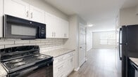 This single-floor unit offers a clean, modern aesthetic throughout its thoughtfully designed layout. The kitchen is a standout feature, showcasing crisp white shaker-style cabinetry with brushed nickel hardware, light granite countertops, and a classic white subway tile backsplash. Black appliances, including a range and over-the-range microwave, provide a sharp contrast against the bright cabinetry. Wood-look plank flooring extends throughout the kitchen and connects seamlessly to the open living area, which is bathed in natural light from a window fitted with horizontal blinds. The living space is generously proportioned with neutral gray walls, white trim, and flush-mount lighting, creating a bright and versatile environment. A dedicated entry area provides a welcoming transition into the main living space. The bedroom is carpeted for comfort and features a spacious closet with a hanging rod, offering ample storage. The bathroom includes a full tub and shower unit with chrome fixtures and a clean, all-white finish. Throughout the unit, consistent neutral tones, modern finishes, and practical design choices come together to create a comfortable and functional living environment.