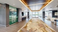 Located at 7971 S Sixth St in Oak Creek, Wisconsin, Emerald Row Oak Creek presents a thoughtfully designed communal amenity floor that sets a high standard for residential community living. The grand entrance lobby welcomes visitors through floor-to-ceiling glass doors framed by expansive windows, flooding the space with natural light and offering views of the surrounding greenery. A boldly branded green accent wall and an elegantly patterned area rug establish a striking first impression as guests move through the corridor toward the interior amenities.

The two living room areas are carefully appointed for both comfort and style. One features a curved white sectional sofa, a sleek pendant chandelier, a marble-topped coffee table, and textured grey wall panels, creating an inviting lounge atmosphere. The second living area showcases a white stacked-stone fireplace, built-in display shelving, rich wood accents, and curated furnishings atop a vibrant abstract rug, adding warmth and sophistication.

A central bar-height lounge area with white countertops, upholstered seating, dark wood cabinetry, and a wall-mounted television serves as an ideal social hub. Outside, a generously sized outdoor pool is bordered by a spacious sundeck lined with lounge chairs, complemented by a courtyard terrace featuring seating and landscaped planters, all set against the building's contemporary façade of contrasting white panels and warm wood cladding.