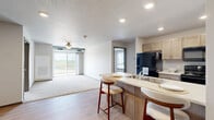 Located in Waukee, Iowa, this two-bedroom, two-bathroom unit offers a well-organized single-floor layout designed for comfortable everyday living. The kitchen is outfitted with light cabinetry, a full suite of black appliances, and a light-toned countertop peninsula with bar seating — an ideal setup for casual dining or entertaining. Hardwood-style flooring runs through the kitchen and common areas, while plush carpet adds warmth to the bedrooms and living room.

The living room opens to a private balcony through a sliding glass door, offering open views of the surrounding Iowa landscape — a standout feature of the space. Both bedrooms are carpeted and well-lit, with the primary bedroom featuring windows that let in natural light and views of the outdoors. Exposed ductwork runs along the upper walls, adding an industrial accent to the otherwise clean, neutral interior.

Each bathroom is finished with wood-toned vanities, light stone-style countertops, a full soaking tub with shower, and hardwood-style flooring. A dedicated in-unit laundry room includes a full-size washer and dryer alongside overhead shelving for added storage. The space also includes a closet for additional organization, rounding out a practical and comfortable floor plan.
