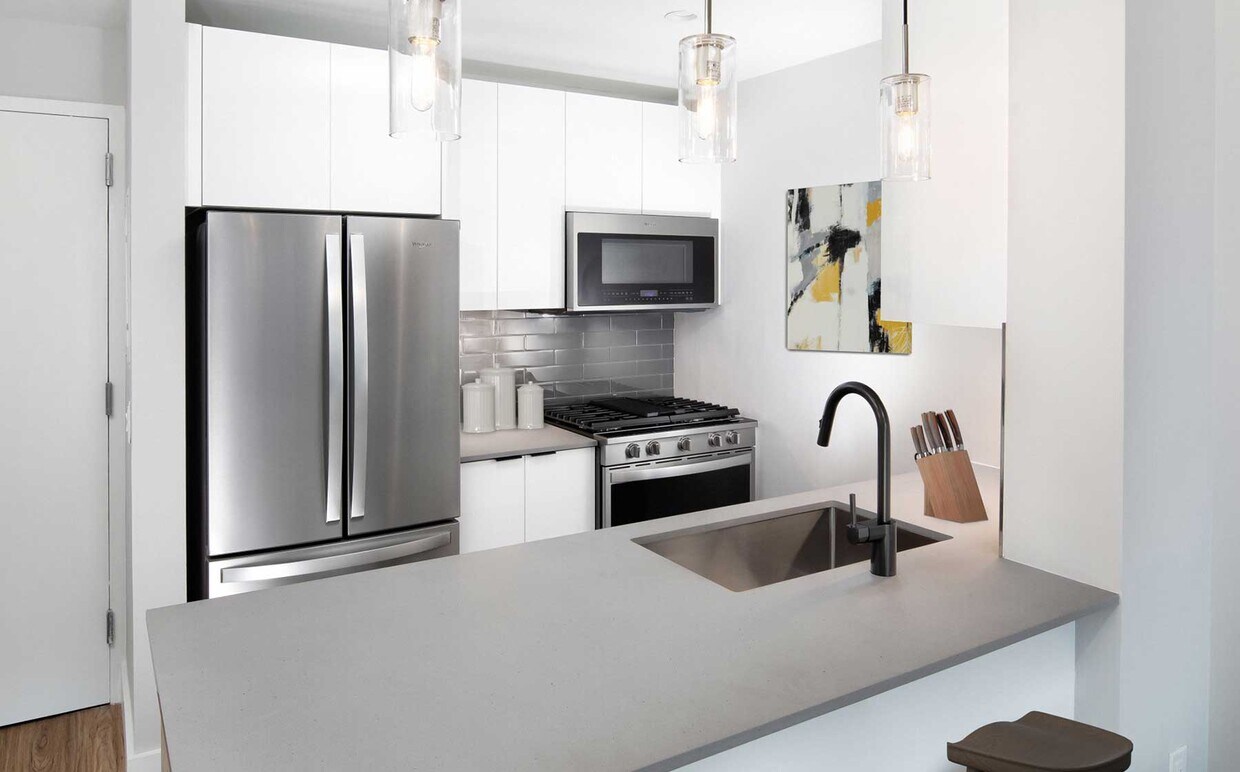 Cocina renovada del Paquete I con electrodomésticos de acero inoxidable, gabinetes blancos, salpicadero de azulejos grises, encimeras de cuarzo gris y pisos de superficie dura (imágenes representativas) - Avalon Riverview