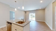 Located at 17151 Windward Blvd in Milford, Delaware, this single-floor residence offers a well-designed, open layout with a neutral color palette and consistent finishes throughout. The kitchen serves as a central highlight, featuring granite countertop surfaces, a central island with an undermount sink, crisp white shaker cabinetry, a classic subway tile backsplash, and a full suite of stainless steel appliances including an electric range, microwave, and refrigerator. Pendant lighting over the island and recessed ceiling lights add layers of illumination. The kitchen flows naturally into a bright living area, which benefits from sliding glass doors that invite abundant natural light and provide direct outdoor views. Hardwood-style flooring runs throughout the main living and kitchen areas, while plush carpeting extends into each bedroom. The bedrooms are generously proportioned, each equipped with ceiling fans and large windows that frame green outdoor scenery. Two bathrooms serve the home: one with a soaking tub and white vanity, and a second with a walk-in shower and light cabinetry. The overall ambiance is clean, modern, and move-in ready, with a cohesive design that prioritizes comfort and functionality.