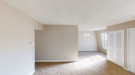 This single-floor residence offers a straightforward and functional layout designed for comfortable everyday living. The open living and dining area is generously proportioned, featuring warm neutral-toned walls, plush wall-to-wall carpeting, and a textured ceiling. A modest chandelier anchors the dining area, while large windows allow natural light to pour in, creating a bright and welcoming atmosphere throughout. The entry area provides a practical transition into the main living space, also finished with carpet and a multi-pane window that fills the room with daylight. The kitchen is efficiently arranged with white cabinetry accented by gold-tone hardware, a gas range, a double-basin sink set into a continuous countertop, and a dishwasher. Light tile flooring and overhead ventilation complete the space. The bedrooms are carpeted and finished with the same neutral palette, each featuring windows that bring in ample natural light and views of the surrounding exterior. The bathroom includes a full tub and shower combination with white tile surround, a toilet, and tile flooring, providing all essential amenities. Overall, the space presents a clean, neutral canvas well-suited for a variety of furnishing styles and personal touches.