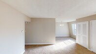 This single-floor residence offers a straightforward and functional layout designed for comfortable everyday living. The open living and dining area is generously proportioned, featuring warm neutral-toned walls, plush wall-to-wall carpeting, and a textured ceiling. A modest chandelier anchors the dining area, while large windows allow natural light to pour in, creating a bright and welcoming atmosphere throughout. The entry area provides a practical transition into the main living space, also finished with carpet and a multi-pane window that fills the room with daylight. The kitchen is efficiently arranged with white cabinetry accented by gold-tone hardware, a gas range, a double-basin sink set into a continuous countertop, and a dishwasher. Light tile flooring and overhead ventilation complete the space. The bedrooms are carpeted and finished with the same neutral palette, each featuring windows that bring in ample natural light and views of the surrounding exterior. The bathroom includes a full tub and shower combination with white tile surround, a toilet, and tile flooring, providing all essential amenities. Overall, the space presents a clean, neutral canvas well-suited for a variety of furnishing styles and personal touches.