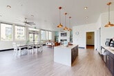 Located at 1601 E 121st Ave in Northglenn, Colorado, this well-appointed community clubhouse spans a single floor and offers a thoughtfully designed open-concept layout. The heart of the space is a fully equipped kitchen featuring dark navy cabinetry, a white subway tile backsplash, stainless steel appliances, and a large central island with bar seating — all illuminated by a striking cluster of copper pendant lights that add a warm, contemporary touch. Light wood-style flooring flows seamlessly throughout, unifying the kitchen, dining, and living areas. The dining area accommodates a large table and benefits from floor-to-ceiling windows that flood the space with natural light and offer views of the surrounding neighborhood. The living area is anchored by a shiplap-clad accent wall housing a wide linear fireplace and a mounted flat-screen TV, complemented by ceiling fans and open shelving. A cozy lounge nook adjacent to the business center provides additional seating, featuring soft blue accent walls and a relaxed, inviting atmosphere. A separate game and recreation room rounds out the space, complete with a foosball table and additional seating. The overall ambiance is bright, modern, and welcoming — designed to serve as a versatile gathering hub.