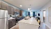Located at 1420 W Diehl Rd in Naperville, IL, this well-appointed one-bedroom, one-bathroom residence offers a thoughtfully designed open-concept layout. The kitchen and living area flow seamlessly together, anchored by a large center island with a striking stone countertop, undermount sink, and pendant lighting overhead. Dark espresso cabinetry pairs elegantly with stainless steel appliances, including a gas range, microwave, and refrigerator, while a white subway tile backsplash adds a clean, modern touch. Light-toned hardwood-style flooring runs throughout the main living areas, enhancing the sense of openness and warmth. The living room is bathed in natural light from multiple windows dressed with navy drapes, and features soft blue-gray accent walls that create a calm, inviting ambiance. The bedroom offers plush carpeting, a ceiling fan, a bold teal accent wall, and a window with warm-toned curtains for a cozy retreat. A dedicated closet provides convenient storage. The bathroom is finished with a glass-enclosed walk-in shower featuring white subway tile, a dark vanity with stone countertop, and wood-look flooring, completing this refined and functional living space.