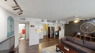 This single-floor unit offers a practical and comfortable layout designed for everyday living. The open-concept living room is a welcoming centerpiece, featuring rich hardwood-style flooring, a ceiling fan with lighting, and a bank of windows dressed in sheer curtains that flood the space with natural light. Track lighting and a decorative accent wall add character to the room.

The kitchen is efficiently designed with white cabinetry, light stone countertops, and stainless steel appliances including a refrigerator, electric range, and dishwasher. A convenient pass-through layout connects the kitchen to the living area, while an adjacent dedicated laundry space houses a full-sized washer and dryer, adding significant everyday convenience.

The unit includes multiple bedrooms, each finished with soft carpeting, ceiling fans, and textured ceilings. One bedroom features a sliding mirrored closet door and a window, offering a bright and functional retreat. The rooms provide comfortable proportions suitable for both sleeping and study or work areas.

Throughout the unit, a textured ceiling treatment is consistent, and the hardwood-style flooring in the main living and kitchen areas contrasts neatly with the carpeted bedrooms, creating a cohesive and functional living environment overall.
