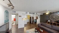 This single-floor unit offers a practical and comfortable layout designed for everyday living. The open-concept living room is a welcoming centerpiece, featuring rich hardwood-style flooring, a ceiling fan with lighting, and a bank of windows dressed in sheer curtains that flood the space with natural light. Track lighting and a decorative accent wall add character to the room.

The kitchen is efficiently designed with white cabinetry, light stone countertops, and stainless steel appliances including a refrigerator, electric range, and dishwasher. A convenient pass-through layout connects the kitchen to the living area, while an adjacent dedicated laundry space houses a full-sized washer and dryer, adding significant everyday convenience.

The unit includes multiple bedrooms, each finished with soft carpeting, ceiling fans, and textured ceilings. One bedroom features a sliding mirrored closet door and a window, offering a bright and functional retreat. The rooms provide comfortable proportions suitable for both sleeping and study or work areas.

Throughout the unit, a textured ceiling treatment is consistent, and the hardwood-style flooring in the main living and kitchen areas contrasts neatly with the carpeted bedrooms, creating a cohesive and functional living environment overall.