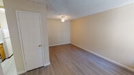 This single-floor unit offers a straightforward, functional layout with a warm, neutral color palette throughout. The living area features wood-look laminate flooring, a flush-mount ceiling light fixture, and a textured popcorn ceiling, creating a clean and practical space. An adjacent dining or flex area includes a built-in pass-through counter with under-cabinet lighting, connecting seamlessly to the galley-style kitchen.

The kitchen is efficiently designed with warm oak cabinetry lining both walls, white countertops, and a full suite of appliances including an electric range, refrigerator, and dishwasher. A range hood provides ventilation above the stove, and light-toned laminate flooring ties the space together.

The bedroom is carpeted and benefits from a window that overlooks a landscaped exterior courtyard, allowing natural light to filter in. A baseboard heater provides zone heating, and the room offers ample wall space for furniture arrangement.

The bathroom is clean and functional, featuring a full-size soaking tub with a shower combo, standard fixtures with chrome hardware, a wall-mounted mirror, and speckled countertop surfaces. White baseboards and beige walls maintain the unit's consistent, understated aesthetic throughout.