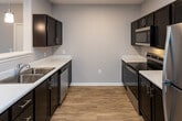 Located at 651 Rain Forest Rd in Knoxville, Tennessee, this single-floor residence offers a clean, modern design with a thoughtfully planned open-concept layout. The main living area is finished with warm wood-look luxury vinyl flooring and neutral gray walls, creating a bright and welcoming atmosphere. Large white baseboards and crisp white door trim provide a polished contrast throughout the space.

The kitchen is a standout feature, showcasing rich dark espresso cabinetry paired with bright white countertops for a striking two-tone aesthetic. Stainless steel appliances, including a refrigerator and dishwasher, complement the space, while a peninsula with pendant lighting connects the kitchen to the living area, making it ideal for entertaining. A double stainless steel sink and built-in microwave add to the kitchen's practical appeal.

The bedroom offers a comfortable retreat with soft carpeting underfoot, a ceiling fan with integrated light fixture, and a window with blinds that allow for natural light. An adjacent closet with built-in shelving provides ample storage. The bathroom is finished with a dark vanity cabinet topped with a white countertop, a large mirror with overhead lighting, and wood-look flooring that ties cohesively to the rest of the unit. The overall design balances contemporary style with everyday functionality.