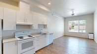 This thoughtfully designed one-bedroom, one-bathroom unit offers a clean, modern aesthetic across a single floor. The open-concept living and kitchen area is bright and welcoming, featuring light wood-style flooring, crisp white walls, and a ceiling fan that enhances the airy atmosphere. A large window in the living area fills the space with natural light and provides views of the surrounding greenery.

The kitchen is efficiently laid out along one wall and includes white cabinetry extending to the ceiling for ample storage, a light-toned countertop, a double-basin sink, a full-size refrigerator, an electric range with overhead ventilation, and a dishwasher — all finished in white for a cohesive look. Recessed lighting above the kitchen adds functional illumination.

The bedroom is a well-proportioned retreat featuring plush carpet flooring, dual windows that invite natural light, a ceiling fan, and a built-in closet with double panel doors. The room's neutral palette creates a calm, comfortable environment.

The bathroom is clean and functional, offering wood-style flooring, a single-sink vanity with a light stone countertop, a large mirror, and a shower-tub combination. Two additional closets provide convenient storage throughout the unit, maximizing the practical use of the overall footprint.