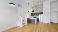Located at 2801 S Pennsylvania St in Indianapolis, IN, this two-story residence offers three bedrooms, one bathroom, and two closets across a thoughtfully designed floor plan. The main floor hosts the majority of the living space, featuring an open-concept layout with warm luxury vinyl plank flooring and crisp white walls that lend a clean, modern aesthetic throughout.

The kitchen is a standout feature, showcasing dark gray cabinetry, a striking geometric-patterned accent wall, stainless steel appliances including a refrigerator, range, and microwave, and a quartz waterfall peninsula with an undermount sink and matte black fixtures. Stylish pendant lights add a contemporary touch overhead.

The living area benefits from soaring ceilings and multiple windows that invite abundant natural light. The bedrooms are bright and well-proportioned, with the primary bedroom offering generous space and large windows framing outdoor views. Each room continues the cohesive wood-tone flooring and neutral palette.

The bathroom is finished with large hexagonal marble-look floor tile, a tub/shower combo, and matte black hardware for a refined contrast. A wall-mounted mini-split system ensures efficient climate control. A staircase with white-painted railings connects the main floor to the upper level, completing this well-appointed urban residence.