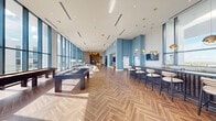 This upscale amenity floor is designed to impress, blending refined materials with open, light-filled spaces throughout. The striking herringbone-patterned wood flooring sets the tone upon entry, carrying through a series of interconnected social areas. Floor-to-ceiling glass curtain walls flood the interior with natural light and frame panoramic skyline and waterfront views, creating a seamless connection between indoors and out.

The expansive game lounge features a full-size billiards table and shuffleboard, anchored by sweeping views through oversized windows. A dedicated lounge area provides comfortable seating, while a built-in media nook with a large-format display and a warm wood-paneled accent wall offers a more intimate retreat. Elevated ceilings throughout amplify the sense of grandeur.

The gourmet kitchen and entertaining bar is a standout feature, showcasing a dramatic slab marble backsplash, rich wood cabinetry, slate-blue lower cabinets with brass hardware, premium stainless appliances, and an expansive marble island with bar seating beneath sculptural pendant lighting. An adjacent dining area completes the entertaining ensemble.

Wide glass doors open directly onto an outdoor terrace with views of the water and surrounding landscape, offering al fresco dining and lounge space. Vertical wood slat accent walls and muted blue-grey tones throughout tie the design together with a polished, contemporary aesthetic.