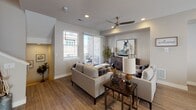 This three-story residence offers a thoughtfully designed layout spread across multiple levels, connected by carpeted stairs with clean white railings and a convenient entryway coat hook station. The main living area is warm and inviting, featuring wood-look flooring, recessed lighting, and a ceiling fan. Large sliding glass doors open to a private balcony, allowing natural light to pour in and providing outdoor views of the surrounding neighborhood. The kitchen is well-equipped with rich dark wood cabinetry, light quartz countertops, a mosaic tile backsplash, stainless steel appliances, and a breakfast bar island with pendant lighting — complemented by an adjacent dining area. The primary bathroom is generously proportioned, offering a long dual-sink vanity with dark wood cabinetry, a glass-enclosed shower, built-in shelving, and direct access to a walk-in closet. A secondary bathroom features a full tub-shower combination with light wood-look flooring. The bedrooms are carpeted and bright, each with wide windows fitted with blinds and ceiling fans for added comfort. Throughout, the neutral warm-toned palette, recessed lighting, and consistent wood-look flooring create a cohesive and modern living environment.