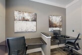 Located at 3378 Greenbriar Pkwy SW in Atlanta, GA, this single-room office is a thoughtfully designed workspace that balances functionality with aesthetic appeal. The room features neutral gray walls, patterned carpet tiles, and clean white trim, creating a polished and professional atmosphere throughout.

The office is equipped with multiple dark-surfaced workstations and ergonomic task chairs, providing ample space for collaborative or individual work. A built-in counter with warm wood cabinetry along one wall offers additional workspace and storage, while a multifunction printer station adds practical utility. A glazed door connects the office to a larger, bright communal area, allowing natural light to filter in and maintaining a sense of openness.

A large window fitted with horizontal blinds serves as the focal point of the room, providing controllable natural light and a bright, airy feel. The walls are adorned with curated abstract artwork — large-scale canvas paintings in muted earth tones and a collection of sculptural wall pieces with a textured, concrete-like quality — lending a refined, gallery-like character to the space.

Recessed and track lighting overhead ensures well-distributed illumination throughout the day. The overall design strikes a balance between a productive work environment and an inviting, design-forward aesthetic.