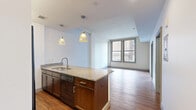 Located in the heart of downtown Columbus at 8 E Long St, this one-bedroom, one-bathroom unit offers a well-designed layout across a single floor. The open-concept kitchen and living area serves as the centerpiece of the space, showcasing rich hardwood flooring, crisp white walls, and abundant natural light from large windows with city views. The kitchen is appointed with warm, dark-stained cabinetry, granite countertops, and black appliances including a side-by-side refrigerator with ice dispenser, electric range, and built-in microwave. A peninsula with an integrated sink and pendant lighting above provides both additional prep space and a casual dining option. The living area benefits from the open flow and natural light streaming in through oversized windows that frame views of Columbus's urban skyline. The bedroom is a comfortable, carpeted retreat featuring large windows that continue the theme of abundant natural light and city views. The full bathroom is finished with large-format marble-look tile flooring, a dark wood vanity with granite countertop, and a well-lit mirror. A utility room rounds out the functional spaces within this efficiently designed urban unit.