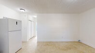Located at 1221 W 66th St in Hialeah, Florida, this single-story, two-bedroom, one-bathroom home offers a straightforward and functional layout. Throughout the space, polished terrazzo flooring provides a classic Florida aesthetic with a durable, easy-to-maintain surface. Crisp white walls and ceilings keep the interior feeling clean and bright.

The open living and kitchen area flows seamlessly, with the kitchen featuring dark cabinetry contrasted by a black subway tile backsplash, light countertops, and a full-size white refrigerator. Flush-mount ceiling lights illuminate the shared space effectively.

The generously sized primary bedroom is the standout room, offering ample space and a large sliding-door closet. A wall-mounted air conditioning unit and a window with blinds allow for climate control and natural light. The second bedroom is similarly appointed, with a window that brings in outside views and ventilation.

The bathroom showcases retro-style light blue square wall tiles, a combined tub and shower with a handheld showerhead, a safety grab bar, and a small frosted window for natural light and privacy. The mosaic tile shower floor adds a classic touch.

The entry area features a solid front door and a window, creating a welcoming and naturally lit foyer. Overall, the home presents a compact yet efficiently organized living space suited for comfortable everyday living.