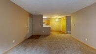 This single-floor unit in Council Bluffs, Iowa, offers a practical and well-organized layout across multiple rooms. The open living area greets residents at entry, featuring neutral-toned carpet, warm beige walls, and a ceiling fan overhead. A peninsula counter visually separates the living space from the kitchen, which is outfitted with warm oak cabinetry, white appliances including a range, refrigerator, and dishwasher, a double-basin sink, and wood-look flooring that adds a clean, durable finish underfoot.

A hallway connects the living area to the private rooms. The bedrooms are carpeted and feature textured ceilings, natural light from windows with blinds, and walk-in or reach-in closets with built-in shelving. One bedroom includes a sliding glass door that opens to a walled outdoor area, providing a private exterior space. Two bathrooms serve the unit; one includes a single-sink vanity with oak cabinetry and a tub/shower combination, while the second features a similar vanity setup with a lighted mirror and a separate shower. A dedicated laundry closet houses a stacked washer and dryer unit alongside additional cabinet storage, completing this functional single-level home.