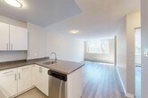 Located at 11005 98 Ave NW in Edmonton's Grovenor neighbourhood, this one-bedroom, one-bathroom unit offers a practical and well-appointed single-floor layout. The open-concept kitchen and living area form the heart of the unit, where a peninsula counter with a dark granite-style surface and an undermount sink defines the kitchen space. White cabinetry provides ample storage, and stainless steel appliances — including a refrigerator and electric range — complete the functional kitchen setup. Light vinyl plank flooring runs throughout the unit, lending a clean and modern aesthetic. The living area benefits from natural light, with large windows offering leafy tree views and a baseboard heating system ensuring year-round comfort. Neutral warm-toned walls throughout create a cohesive and inviting atmosphere. The bedroom is a comfortable size, featuring a built-in closet and wall sconce lighting, with direct access to the bathroom. The bathroom is finished with crisp white subway tile surrounding a full soaker tub and shower combination, paired with chrome fixtures for a clean, classic look. Textured ceilings add a subtle layer of character throughout the unit. Overall, the space presents a straightforward, functional layout ideal for single occupants or couples.