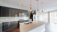 Located in Atlanta, GA, this well-appointed single-floor residence offers four bedrooms, two bathrooms, and a thoughtfully designed open-concept layout. A welcoming hallway with dark hardwood flooring and flush ceiling lighting leads into the main living areas. The kitchen is a standout feature, showcasing high-gloss gray cabinetry, stainless steel appliances, a white subway tile backsplash, and a large quartz-topped island illuminated by striking globe pendant lights. Track lighting overhead adds both function and modern flair. The combined kitchen and living area flows seamlessly, with the living room offering large sliding glass doors and windows that frame lush outdoor views and flood the space with natural light. A ceiling fan adds comfort to this expansive area. The four bedrooms include a generously sized primary suite with plush carpeting, dual windows, and sliding door access to the outdoors. Additional bedrooms feature carpet or hardwood flooring and ample window exposure. The primary bathroom is finished with large-format tile flooring, a sleek dual-vanity with gray cabinetry, a soaking tub, and direct access to a walk-in closet equipped with wire shelving. Throughout, neutral tones and clean architectural lines create a cohesive, contemporary ambiance.