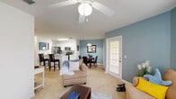 Located at 2301 Academy Cir W in Kissimmee, Florida, this single-floor residence offers a thoughtfully designed layout that maximizes comfort and functionality. The open-concept living and dining area is anchored by soft carpet flooring, ceiling fans, and large windows dressed with patterned curtains that invite natural light. The living room features a calming blue-gray accent wall, while the adjacent dining area mirrors this palette, creating a cohesive, relaxing atmosphere throughout the shared space.

The kitchen is well-equipped with white cabinetry, stainless steel appliances including a refrigerator, microwave, and electric range, complemented by wood-look flooring and a breakfast bar with seating — ideal for casual dining. A double-basin sink and ample counter space make this kitchen both practical and inviting.

The spacious bedroom accommodates a full-size bed with ease, offering two windows that flood the room with natural light, plush carpeting, a ceiling fan, and a dedicated closet for storage. The full bathroom features tile flooring, a combined tub and shower, a single vanity with a wide countertop, and clean white finishes throughout. The surrounding green landscaping, visible from the exterior, adds to the overall appeal of this well-rounded Kissimmee residence.