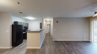 This single-floor residential unit offers a practical and well-designed layout with consistent hardwood-style flooring flowing throughout the entire space. The kitchen is equipped with dark cabinetry, black appliances including a full-size refrigerator and range, and dark countertops that extend to a peninsula breakfast bar, which opens directly to the adjacent living and dining area. The open-concept design between the kitchen and main living space creates a connected, functional flow ideal for everyday living.

The living area is spacious and bright, featuring a ceiling fan with light fixture and a large sliding glass door fitted with vertical blinds that allows natural light to fill the room. A hallway connects the living area to the private rooms, each featuring ceiling fans and windows with blinds that bring in additional natural light.

Two bathrooms serve the unit. One features a pedestal sink, a framed mirror, and an accessible tub/shower combination with sturdy grab bars — a thoughtful design detail. The second bathroom includes a vanity with storage, a framed mirror, and hardwood-style flooring. The hallway also provides access to what appears to be an in-unit laundry area. Neutral wall tones and clean white trim complete the understated, move-in-ready aesthetic throughout.