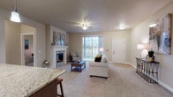 This single-floor residence offers a thoughtfully designed layout that balances comfort and functionality throughout. The living room serves as the centerpiece of the home, featuring a stone-accented fireplace with a classic white mantel, ceiling fan, and large sliding glass doors that invite natural light and provide views of the surrounding outdoor scenery. Soft carpeting and warm neutral tones create a welcoming ambiance throughout the main living areas.

The kitchen is equipped with rich wood cabinetry, granite countertops, stainless steel appliances including a refrigerator, electric range, and microwave, and light hardwood-style flooring. A dedicated pantry provides additional storage. Adjacent to the kitchen, a dining area with hardwood-style flooring accommodates a full dining set and is brightened by a window with blinds.

The spacious bedroom features a ceiling fan, a window with outdoor views, and plush carpeting, while a generous walk-in closet with wire shelving provides ample storage. A secondary living or flex room offers additional versatile space with carpeting and natural light. The bathroom includes a wood-toned vanity and hardwood-style flooring. A dedicated in-unit laundry room houses a full-size washer and dryer with overhead shelving for added convenience.