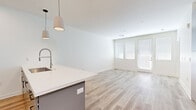 Located at 500 W Camelback Rd in Phoenix, Arizona, this thoughtfully designed one-bedroom, two-bathroom residence offers a bright and modern living experience on a single floor. The open-concept kitchen and living area serves as the heart of the home, featuring light wood-tone flooring, crisp white walls, and abundant natural light streaming through large windows and a glass-paneled door. The kitchen is equipped with stainless steel appliances, including a French door refrigerator, gas range, and built-in microwave, complemented by white cabinetry, gray lower cabinets, a sleek quartz countertop island, and stylish pendant lighting. A built-in desk flanked by gray cabinetry provides a functional workspace within the living area. The bedroom offers soft carpeting, a sunlit window with blinds, and a clean, neutral palette. The bathrooms are finished with contemporary gray vanities, illuminated mirrors, and a glass-enclosed walk-in shower with white tile surround and chrome fixtures. A dedicated entrance area and well-appointed hallway complete this efficiently designed residence. The overall ambiance is clean, modern, and move-in ready.