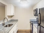 Located at 2100 Wilson Rd in Knoxville, Tennessee, this single-floor residence offers a well-designed layout with a clean, neutral aesthetic throughout. The living area serves as the heart of the home, featuring dark hardwood-style flooring, a classic fireplace with a white mantel, and a sliding glass door that floods the space with natural light and provides direct access to the outdoors. Adjacent to the living area, the galley-style kitchen is thoughtfully appointed with white shaker cabinets, granite-patterned countertops, a stainless steel sink, and black appliances including a range, over-the-range microwave, refrigerator, and dishwasher — all set atop matching hardwood-style flooring. A hallway connects the main living spaces to the private quarters, featuring a convenient closet with built-in shelving and hanging rods for additional storage. The bedroom is generously sized with plush carpeting, natural light from a window with outdoor views, and the added benefit of dual closets offering ample wardrobe space. The bathroom continues the granite-style countertop aesthetic, complemented by a vanity mirror, a bathtub and shower combination, and hardwood-style flooring. Throughout the residence, a cohesive neutral color palette and practical finishes create a comfortable, move-in-ready living environment.