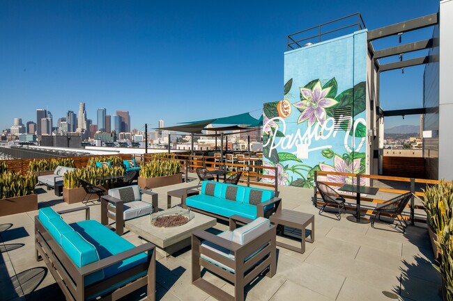 a rooftop patio with blue chairs and tables and a mural on a building - Aliso