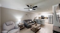 Located at 180 W Dublin Dr in Madison, Alabama, this single-floor residence offers a well-designed layout with a seamless blend of comfort and functionality. The living area features warm, light-toned luxury vinyl plank flooring, crown molding, a textured ceiling, and a ceiling fan with integrated lighting. Natural light filters in through blinds-covered windows, creating a bright and inviting atmosphere. The space flows directly into a peninsula-style kitchen equipped with white shaker cabinetry, granite-look countertops, a mosaic tile backsplash, stainless steel appliances including a refrigerator, microwave, and range, and a double-basin sink with a pull-down faucet. A breakfast bar with seating connects the kitchen to the living area. The bedroom is carpeted and comfortably sized, featuring a ceiling light fixture, a window with outdoor views, and ample space for furnishings. Two bathrooms serve the residence, each featuring white cabinetry, granite-look countertops, vanity lighting, large mirrors, and tub-shower combinations. One bathroom includes a double-sink vanity, offering added convenience. Throughout, the neutral color palette and consistent finishes provide a cohesive, move-in-ready environment.