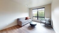 Unit 304 is a thoughtfully designed one-bedroom, one-bathroom apartment offering 610 square feet of modern living space across a single floor. The unit features hardwood-style flooring throughout, neutral-toned walls, and large black-framed windows that fill the space with natural light and offer pleasant outdoor tree views.

The living room is bright and open, anchored by a large picture window with roller shades that frame views of the surrounding greenery. The galley-style kitchen is well-equipped with stainless steel appliances, including a full-size refrigerator, range, and microwave, complemented by gray cabinetry, white countertops, and a single-basin sink beneath pendant lighting.

The primary bedroom spans 180 square feet and features the same large black-framed windows, providing ample natural light and outdoor views. The full bathroom is clean and contemporary, finished with wood-look flooring, a white vanity with chrome hardware, and a tub-shower combination.

A dedicated laundry area houses a stacked Whirlpool washer and dryer unit alongside wire shelving for added storage. A separate closet provides additional organizational space. The overall aesthetic is modern and understated, making Unit 304 a functional and comfortable urban residence.