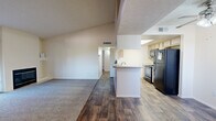This single-story, three-bedroom, two-bathroom home in Tucson's east side offers a well-organized layout designed for comfortable everyday living. The open-concept living and dining area immediately draws attention with its notably tall, vaulted ceilings that lend an airy sense of space. A fireplace anchors one wall of the living room, which features carpet flooring and a sliding glass door leading to a private patio with outdoor views of surrounding greenery.

The kitchen is efficiently arranged in a galley style, featuring light wood cabinetry, a skylight for natural illumination, a breakfast bar peninsula that opens toward the living area, and wood-look flooring. Black appliances, including a full-size refrigerator, range, and dishwasher, complete the functional setup.

The three bedrooms are carpeted and offer generous wall space and good natural light via windows dressed with vertical blinds. The primary bedroom includes a sliding-door closet. Both bathrooms share a consistent design, featuring light wood vanity cabinetry, speckled countertops, large mirrors, and wood-look flooring. One bathroom includes a shower/tub combination.

Hallways connect the rooms efficiently throughout the single-floor layout, creating a cohesive and practical flow.