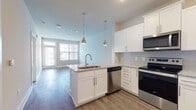This one-bedroom, one-bathroom unit at Annabelle on Main in Duluth, GA offers a well-designed single-floor layout with modern finishes throughout. The open-concept kitchen serves as the heart of the space, showcasing white shaker-style cabinetry, granite countertops, a subway tile backsplash, and a full suite of stainless steel appliances including a range, microwave, dishwasher, and refrigerator. A peninsula with a double-basin sink and dual pendant lights connects the kitchen seamlessly to the living area, which features wood-look flooring and natural light from large windows and a glass-panel door. The bedroom is carpeted for comfort, fitted with a ceiling fan, and receives ample natural light through a sizable window with blinds. The bathroom is finished with a granite-topped vanity, wood-look tile flooring, and a glass-enclosed shower. The consistent use of neutral tones, clean lines, and quality materials throughout creates a cohesive and contemporary ambiance, making this unit a functional and stylish living space in the heart of Duluth.