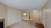 This single-floor residence offers a bright and functional layout designed for comfortable everyday living. The main living area is finished with plush wall-to-wall carpeting in a warm neutral tone, complemented by smooth beige walls and white baseboard trim that lend the space a clean, cohesive aesthetic. A textured popcorn ceiling adds a classic touch overhead, while a ceiling fan positioned toward the dining or secondary living area provides both practical airflow and subtle ambient lighting.

The open floor plan creates a seamless flow between the living and dining spaces, offering a generous sense of openness. A distinctive pass-through window connects the main living area to the kitchen, promoting an inclusive feel while maintaining a clear spatial distinction between rooms. The kitchen features warm wood-toned cabinetry, a white appliance suite, and efficient counter space, making it well-suited for daily meal preparation.

The neutral color palette throughout the space provides a versatile canvas, allowing for a wide range of interior design possibilities. The layout is straightforward and practical, with well-placed electrical outlets and an efficient use of square footage that maximizes livability. Overall, the space presents a tidy, move-in-ready environment with a welcoming and understated character.
